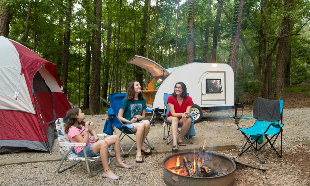 Three girls sitting around a campfire next to a micro trailer