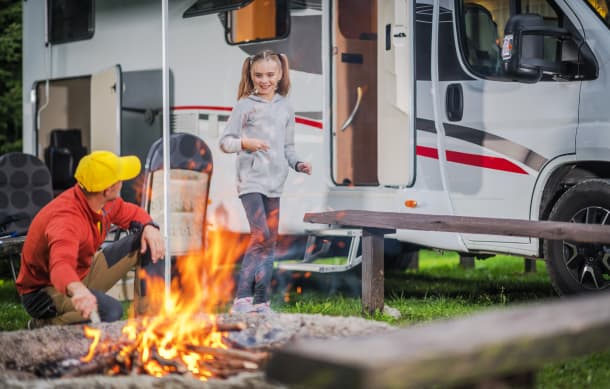 Family next to a campfire and RV in a campground